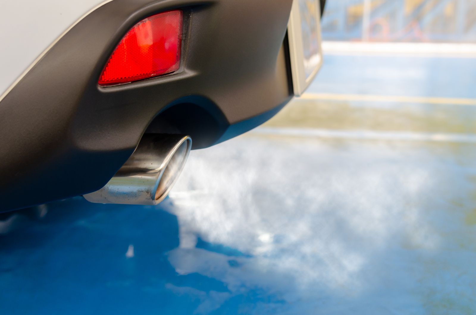 Close-up of a car's rear bumper and chrome exhaust tip with light vapour visible at the outlet