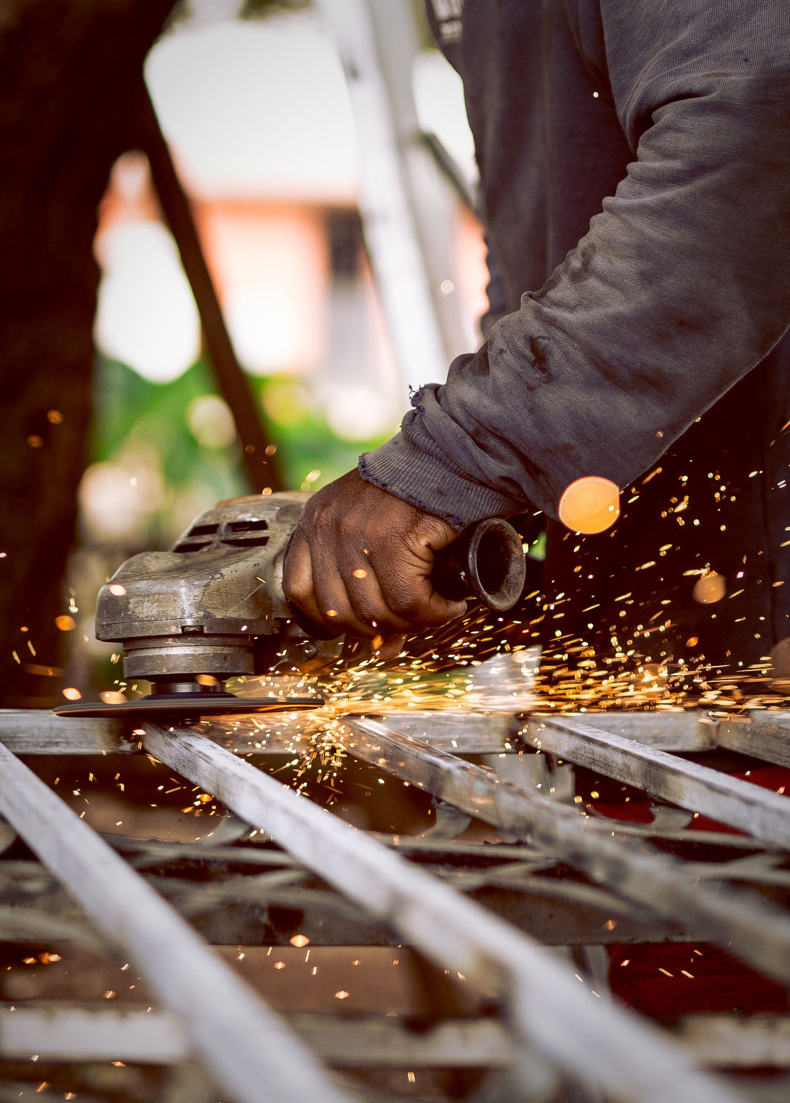 Close-up of a hand operating an angle grinder on a metal frame with bright orange sparks flying